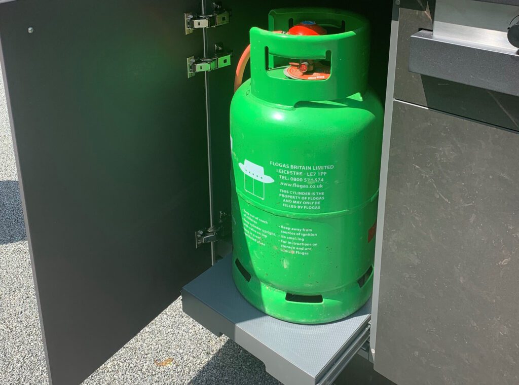 A gas bottle ledge in a cupboard of an outdoor kitchen
