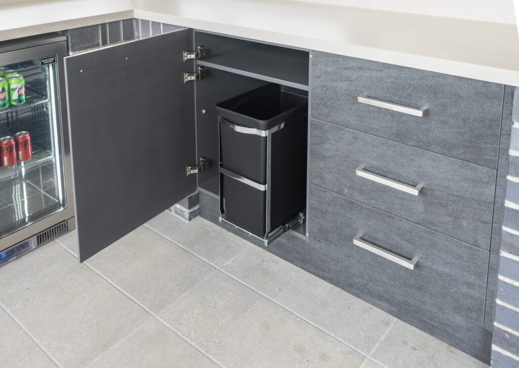 A pull out bin in the cupboard of an outdoor kitchen